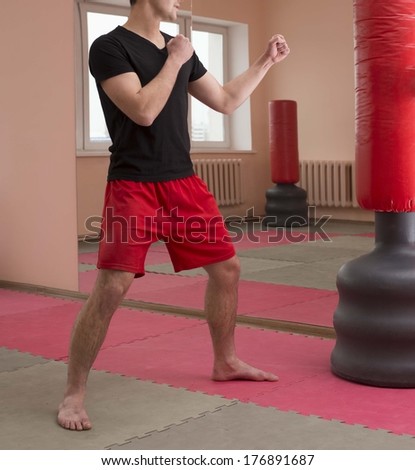 Portrait of young adult latin hispanic man boxer training in gym with blue gloves boxing  punching bag Aggressive male inside wall room against window background