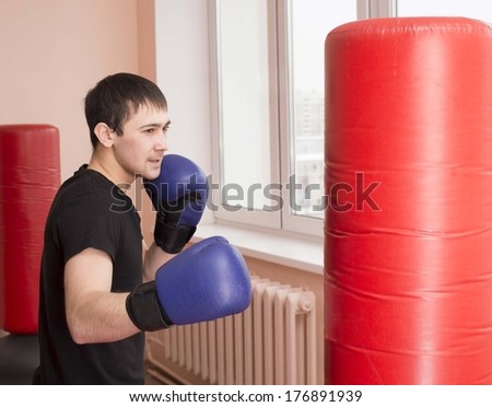 Portrait of young adult latin hispanic man boxer training in gym with blue gloves boxing  punching bag Aggressive male inside wall room against window background