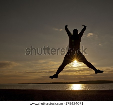 black silhouette of big man in happy jump on orange or yellow under sunset rays cloudy sky and over sea Copy space for inscription Sun between legs The idea lightness freedom flight