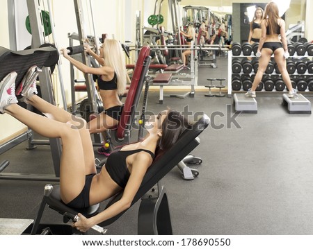 Portrait of three young adult Girls do exercise for legs and hands. in fitness gym on mirror with reflection and window background 3 woman with long blond and brunette hair sitting smiling face