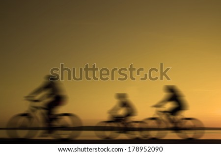 Blurred silhouette of three ( 3 ) people Image of sporty company friends on bicycles outdoors against  yellow sunset beach. Silhouette motion of cyclist along the shoreline coast