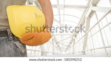 torso and hand in gloves manual worker holding yellow helmet for workers security on metal and glass air above the urban pedestrian crossing highway background