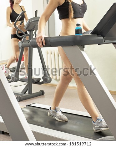 Two young adult sporty women run on machine in the gym centre Couple of girl on Treadmill running inside in fitness gym No face Unrecognizable person