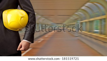 torso and hand engineer holding yellow helmet for workers security with construction paper plans on the background of a new transition buildings of glass and plastic