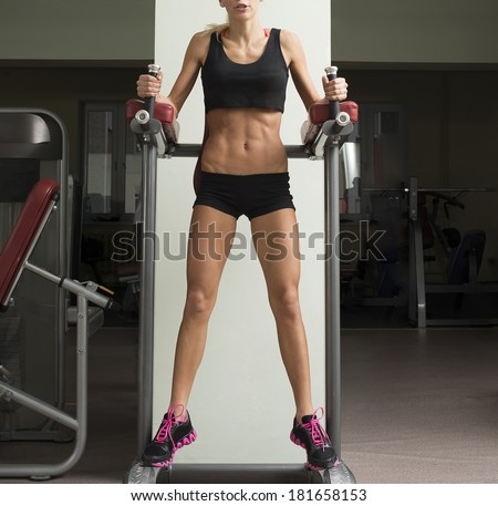 Fitness cut  slim Woman in black short shorts No face. Close-up young adult blond girl with long hair holding simulator for swing press and muscles sexy legs on dark green wall background
