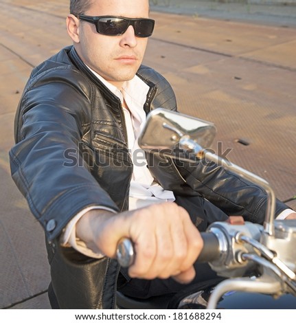 Portrait of Young man in stilish sunglasses and black leather jacket siting chopper holding the steering wheel old rusty metal bridge Copy space for inscription Copy space for inscription Vertical