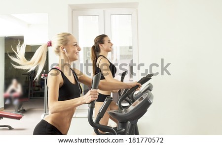 Portrait of Two young adult cut sporty women run on machine in the gym centre Beautiful girls with white headphone inside on on wall and window background