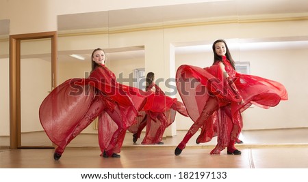 Portrait of two cut young adult girls in red dresses on mirror reflection inside on wall background Full length beautiful woman looking at camera