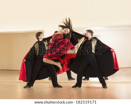 Portrait of three Young adult people One girl and two man dancing passion flamenco  Woman between jumping in long red spanish dress