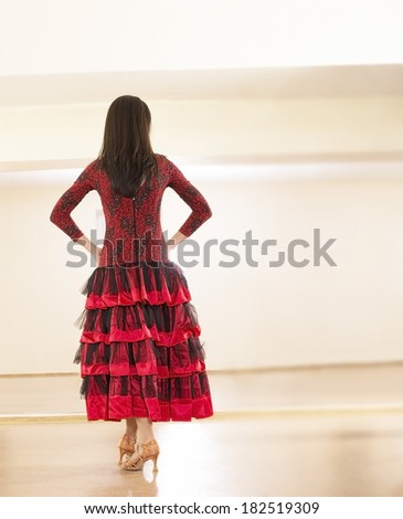 Back view of Beautiful young adult lady woman wearing black and red rose long dress Cut girl with brunette hair full length on high heels indoor with reflection in mirror Unrecognizable person