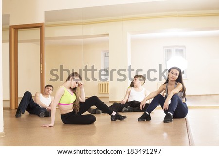 Four tired people sitting on Low section of two women and couple man relaxing in ballet rehearsal room on yellow wall with mirror reflection background