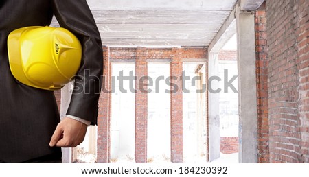 adult engineer inspector hand holding yellow plastic helmet for workers security over texture symmetrical red brick wall New constructed masonry work background No face Copy space for inscription