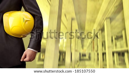 torso and hand engineer holding yellow helmet for workers security against the support beams of the unfinished industrial workshop or room inside Copy space for inscription