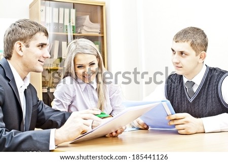 Portrait of business group of three people discussing papers at table in the office with pens in hands