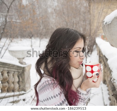 Portrait of young adult latin hispanic girl drinks tea or coffee over cold winter park nature background outdoor Cut Woman with snowflake in brunette long curly hair holding warm red cup