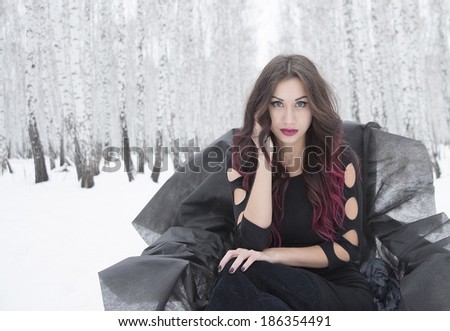 Portrait of Young adult attractive latin hispanic woman in sexy black dress posing over winter snowy forest and snow drift  background