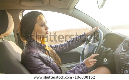 Portrait of beautiful young latin hispanic brunette woman in the new car - indoor keeps the wheel turning around and smiling and looking at the passengers in back seat. The idea of taxi driver