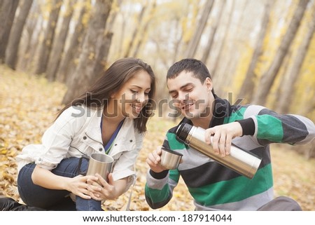 Portrait of Young adult  latin hispanic pair in yellow forest wood sitting on leaves pour and drink hot coffee from a thermos heating in cup copy Space for inscription
