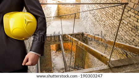 torso engineer hand holding yellow helmet for workers security on the background of a old apartment buildings rusty metal ladder of old abandoned red brick wall