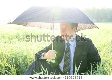 Businessman with umbrella outside on fresh  grass field - protection concept  business man sitting under an shadow on a green meadow on summer forest background
