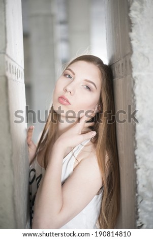 Portrait of Pretty brunette woman in white shirt against an architectural concrete beam background Fashion beautiful dreaming girl looking at camera