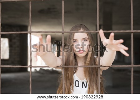 Portrait of beautiful slim girl in jail pull hands ahead on metal lattice  on dark room background Scary woman need help in prison