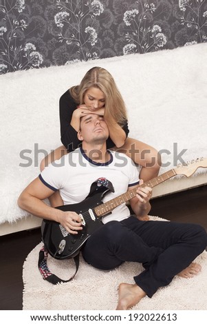 Portrait of  romantic couple with electric guitar inside home interior on black and white wall background Girl based on head his romance boyfriend Man playing music instrument