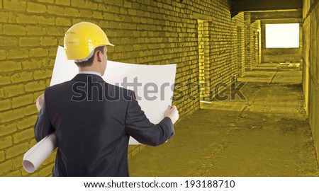 Rear view of architect looking comparing paper plan housing project with building wearing yellow helmet  Back view businessman in perspective long corridor with door and window background