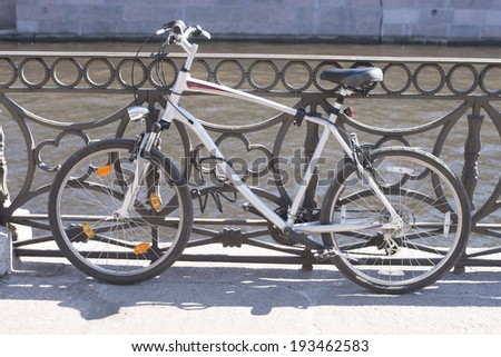 Retro styled Bike locked for parking in european city against metal fence river bridge background