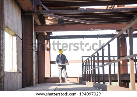 view An architect full length standing on metal floor inside building with blueprints paper plan . Steel frame construction. Focus on rusty fence in perspective