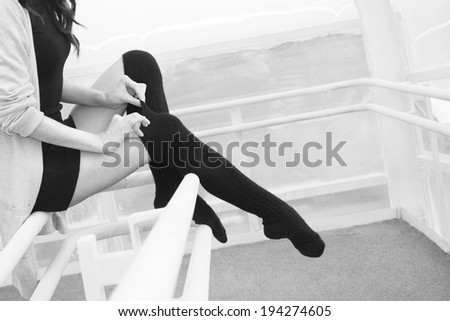 Unrecognizable person No face Woman legs in black pantyhose stockings indoor sits on railing Copy space for inscription Young adult girl wearing short dress and tightens a thin fingers woolen tights