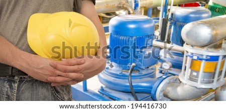Construction worker hands holding yellow plastic helmet  on electric motor pump and pipe background   keep hard hat close-up  Copy space for inscription