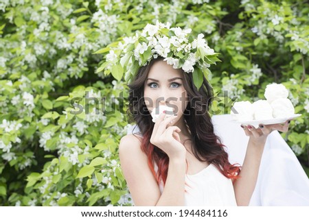 Portrait of beautiful latin hispanic girl sitting with bloom spring wreath in white armchair Cute woman wearing sexy dress has a rest in summer park cafe against blooming apple trees background