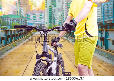 Man's hands standing on old rusty metal bridge and holding modern bicycle on city background, close up photo,