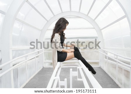Unrecognizable person No face Woman legs in black pantyhose stockings indoor sits on a metal railing Copy space Young adult girl wearing short dress and tightens a thin fingers woolen tights