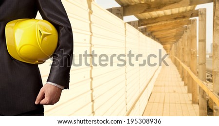 engineer\'s hand holding yellow helmet for workers security on background of metal and wooden fence in perspective on background of evening sunset sky