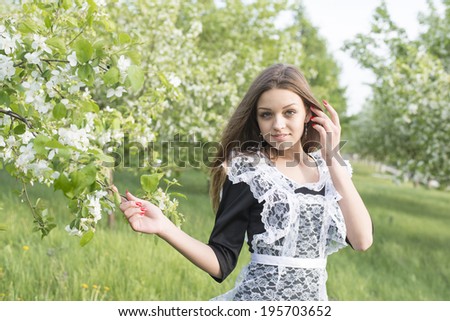 Portrait of young adult caucasian school Girl holding branch with blooming spring flowers on apple tree background. Full length Cute female  standing on fresh green grass