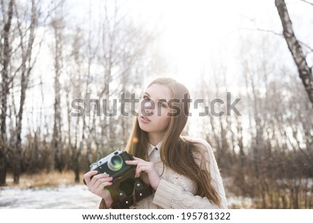 Portrait of pretty young adult girl taking photographs with old vintage retro camera on winter tree and snow background Cute slim woman looking on camera against sun rays and sunset sky background