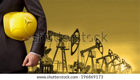 Oil Industry Pump jack with one oil worker in an orange vest with hand holding yellow helmet  torso and hand engineer yellow hardhat for security  No face Unrecognizable person