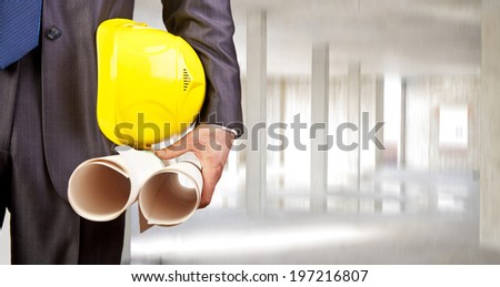 torso engineer holding yellow helmet for workers security and two blueprint over empty new building inside concrete beam in house background Copy Space for inscription