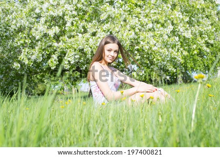Full length portrait of beautiful young woman lying on a meadow against white flower on apple tree Cute slim girl with long brown hair in gray dress looking up and enjoying Copy space for inscription