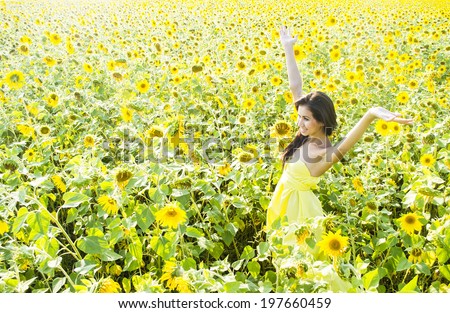 Portrait of Young adult beautiful latin hispanic girl in yellow dress walking with hands raised in sunflower field background Space for inscription Cute slim woman in sunny summer day against flower