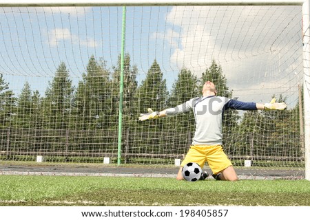 Full length portrait of Goalkeeper in uniform with smiley face defends ball Man standing on fresh green grass football field Copy space for inscription
