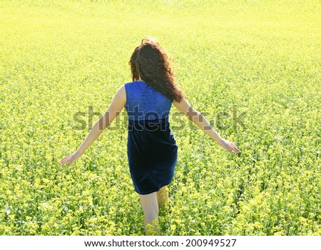 Back view redhead curly young adult woman in yellow raps flower field and blue cloudy sky background Copy space for inscription Girl wearing violet sexy dress No face Unrecognizable person