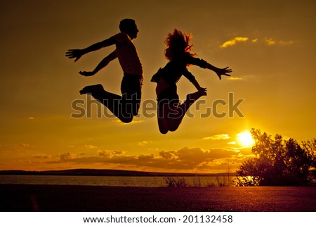 family vacations on the beach Silhouette of a couple - man and woman jumping on the beach on sunset cloudy sky with orange sun background with reflection on yellow water