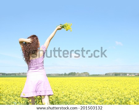 Back view Beautiful caucasian young adult redhead woman in short purple dress with bouquet on summer yellow green flower rape field outdoors sunny day look at far away Copy space for inscription