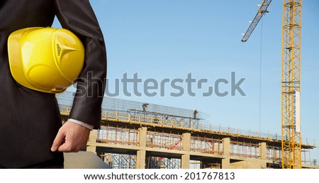 torso engineer hand holding yellow helmet for workers security on background of new highrise apartment buildings and construction cranes on blue sky background  Crane lifts load
