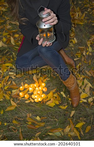young girl with metal lantern with candle light  in hand sitting at autumn dry green and yellow grass No face Unrecognizable person Copy space for inscription
