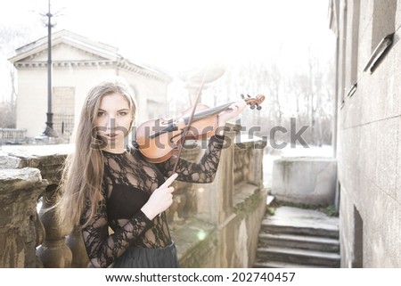 Portrait of Young adult sexy girl with long brown hair with a broken violin on old retro fence and concrete stairway in the Gothic style of classicism Cute slim woman wearing transparent black shirt