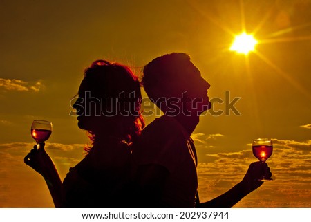Silhouettes of Man and woman clinging glasses of champagne at sunset dramatic yellow sky background Sun rays shine Copy space for inscription